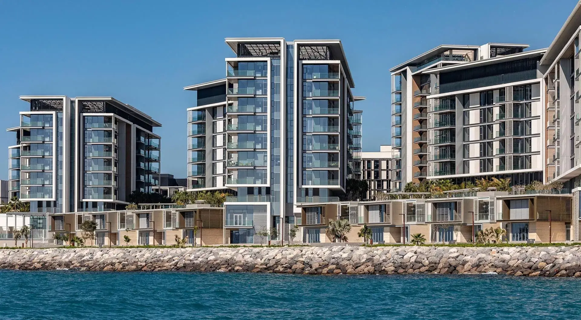 A modern residential development at Bluewaters Island, Dubai, featuring contemporary architecture with glass facades, set against the backdrop of the Ain Dubai (Dubai Eye) Ferris wheel and the waterfront. The image highlights luxury apartments surrounded by landscaped areas and walkways.