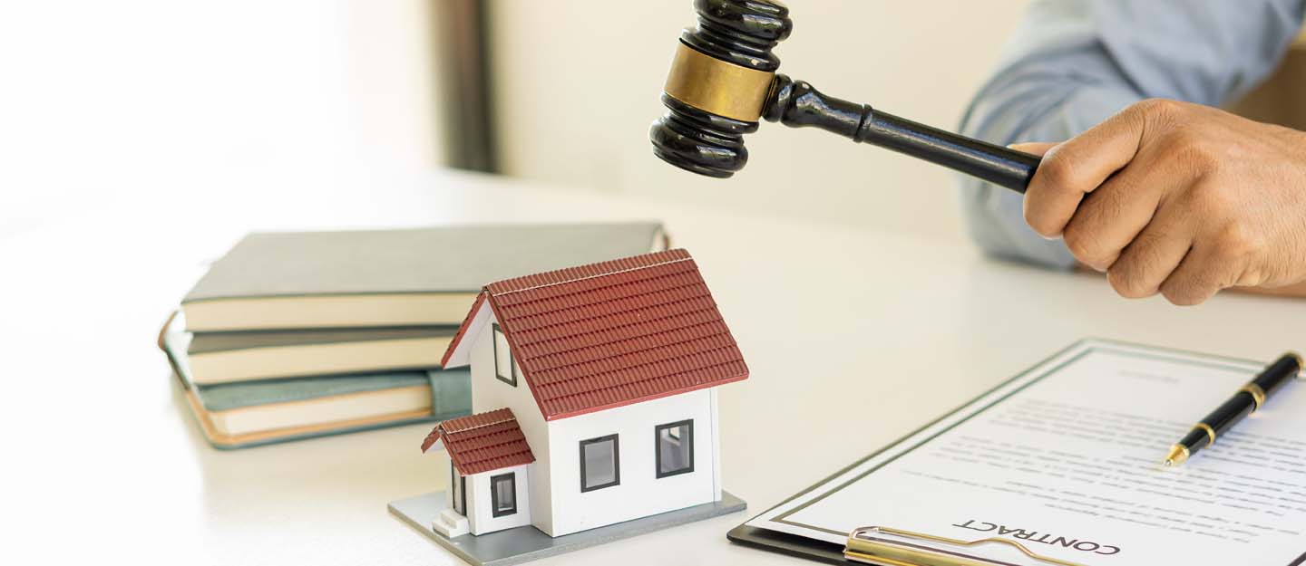 Buying Property on Installment in Dubai A miniature house model on a desk, next to legal documents and a gavel being held by a person, symbolizing property law and real estate transactions.