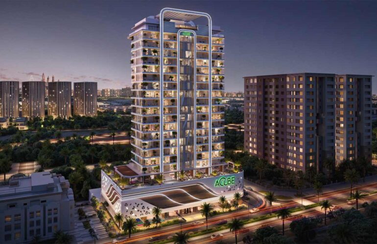 Main view of Vega Residence in Dubai Sports City, taken at night. The illuminated lights showcase the building's beautiful facade, with the main road located in front of the large apartment