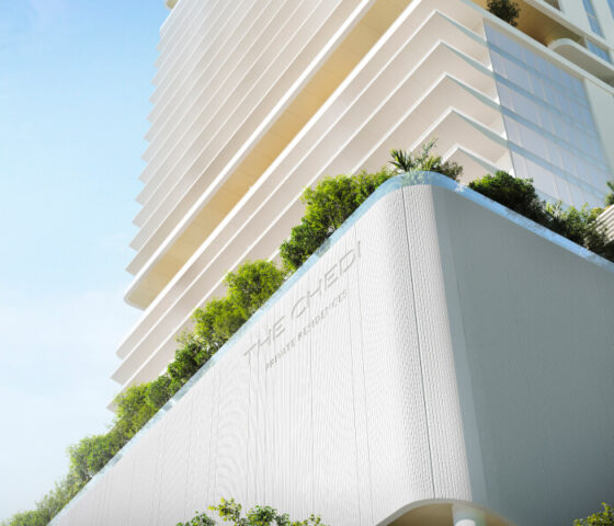 A view of The Chedi Private Residences in Dubai taken from below. Plants are visible at the base of the apartment, and the building extends upwards. The weather is sunny