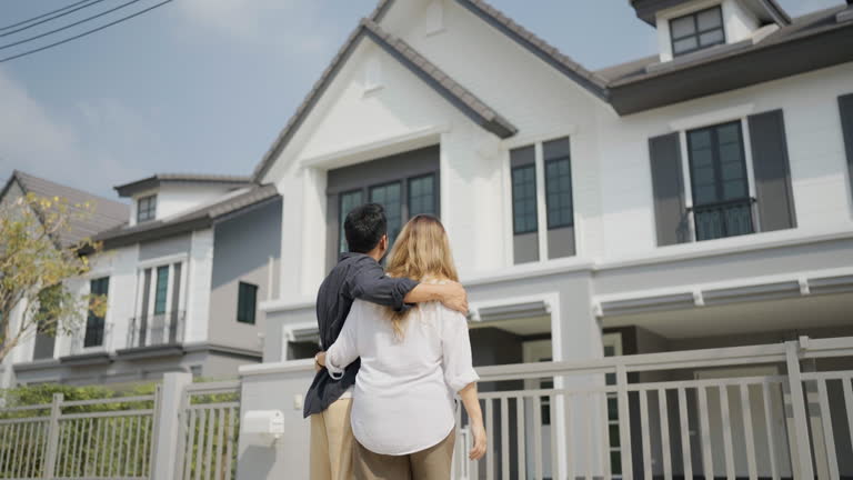 A couple standing together, gazing at a modern house in front of them