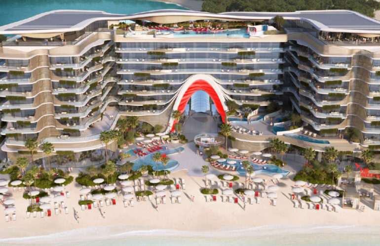 Grand beachfront facade of The Unexpected Hotel Dubai, featuring a signature red architectural arc and luxury beach setup.