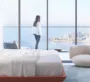 It is a photo of a bed with a person standing next to it and large windows in front of it