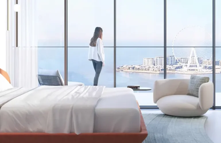 It is a photo of a bed with a person standing next to it and large windows in front of it