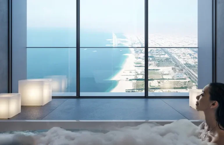 Inside a bathroom where a woman is in a bathtub with a view to the beach