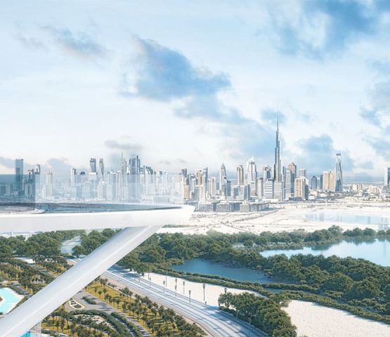 The image appears to showcase a futuristic cityscape with a skyline featuring numerous skyscrapers, including a prominent tall tower that resembles the Burj Khalifa. The foreground includes a modern architectural structure with a sleek, white design, possibly an observation deck or a bridge. Below, there are lush green areas, water bodies, and a network of roads. The sky is mostly clear with some scattered clouds, giving the scene a bright and airy atmosphere.