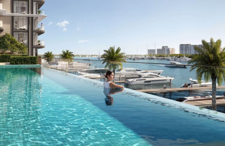 Woman relaxing in an infinity pool at Baystar by Vida in Dubai, with palm trees and yachts in the background.
