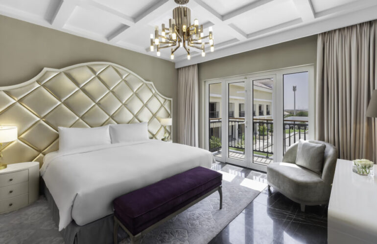 A sophisticated bedroom with high ceilings, plush bedding, and large windows overlooking a private garden at Al Habtoor Polo Resort & Club Dubai.