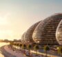Sunset view of organically shaped buildings curving along the waterfront promenade.