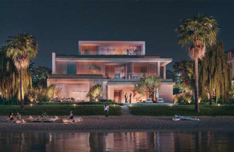 A photo of the front view of a large villa at The Acres Estates in Dubailand, taken at night. In front of the villa, there is a lake.