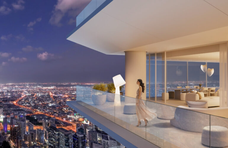 A white balcony at The Chedi Private Residences in Dubai, with a night view of homes and apartments, as a woman or girl looks outside.