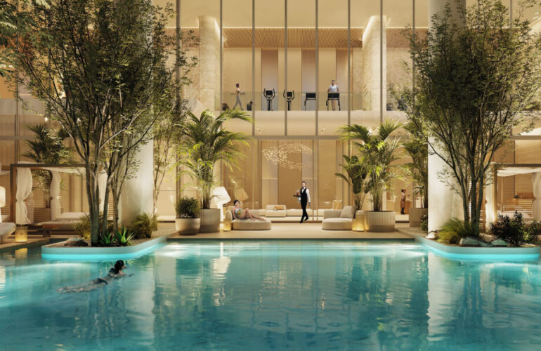 A large pool in the courtyard of a villa at The Chedi Private Residences in Dubai, with the villa illuminated at night. The white villa shines, and the pool area is surrounded by green trees and plants