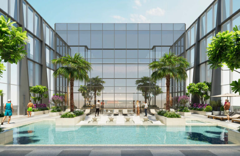 A large pool at The Element at Sobha One Apartments in Dubai, surrounded by small glass walls resembling windows. Palm trees surround the pool, and the sky is clear and blue.