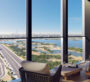 A room at The Element at Sobha One Apartments in Dubai, with two white sofas arranged facing a large window, offering a view of the sea and beach. The weather is sunny.