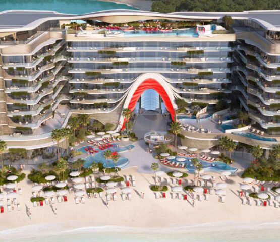 Grand beachfront facade of The Unexpected Hotel Dubai, featuring a signature red architectural arc and luxury beach setup.